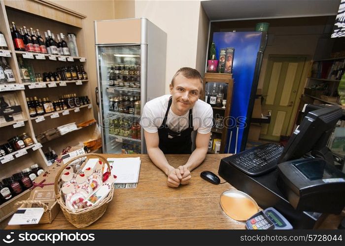 Portrait of salesman leaning at cash counter in supermarket