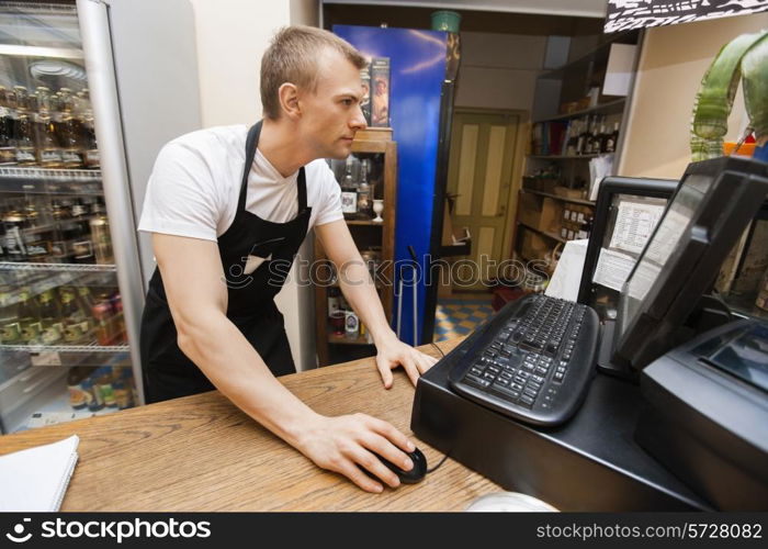 Portrait of salesman using computer at cash counter in supermarket