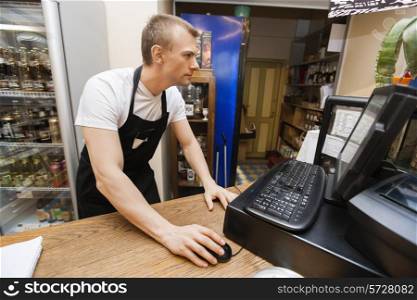 Portrait of salesman using computer at cash counter in supermarket