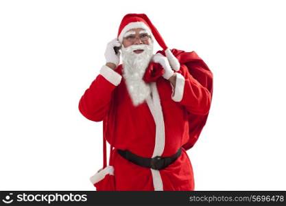 Portrait of Santa Claus talking on mobile phone while carrying sack over white background