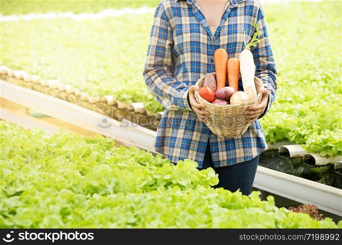 Portrait of satisfied glad asian young woman carrying basket in greenhouse hydroponic organic farm.