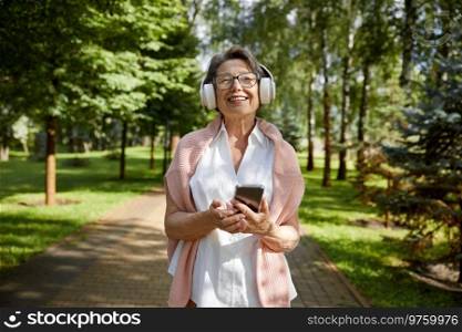 Portrait of satisfied old woman using mobile enjoying summer day while walking in public park. Portrait of satisfied old woman using mobile enjoying summer in park