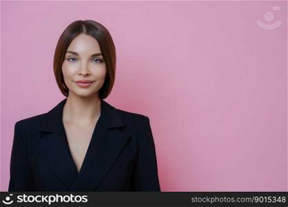 Portrait of satisfied pleasant looking young woman dressed in formal clothes, looks directly at camera, has calm expression, poses against pink background, copy space for your advertisement.