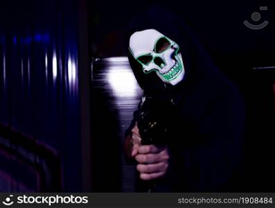 Portrait of scary murderer holding gun and standing in dark place. Crime, Horror and Halloween Concept.