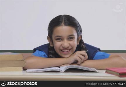 Portrait of school girl leaning on table while studying in classroom