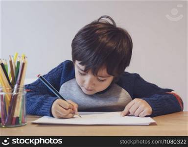 Portrait of school kid boy siting on table doing homework, Happy Child holding blue colour paint,A boy drawing blue colour on white paper at the table,Elementary school and homeschooling concept