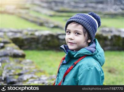 Portrait of School kid explore and learning about history with school trip, Happy child boy wearing hat and winter cloths standing alone with blurry ruins of old abbey background