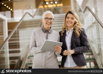 Portrait of senior and young businesswomen standing in office with digital tablet and discuss
