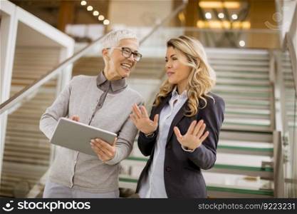 Portrait of senior and young businesswomen standing in office with digital tablet and discuss