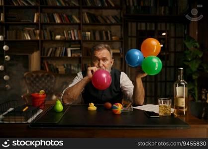 Portrait of senior business man blowing up balloon for success celebration. Grey-haired fashioned mature male boss sitting at work table in home office. Portrait of senior business man blowing up balloon for success celebration
