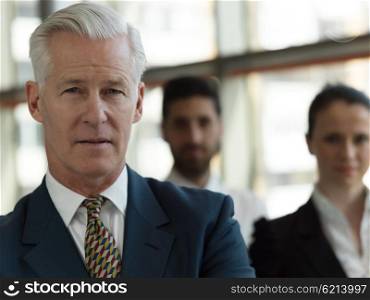 portrait of senior businessman as leader at modern bright office, business team people group in background