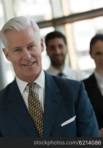 portrait of senior businessman as leader at modern bright office, business team people group in background