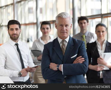 portrait of senior businessman as leader at modern bright office, business team people group in background