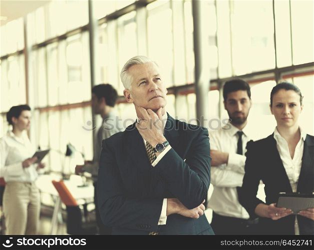 portrait of senior businessman as leader at modern bright office, business team people group in background