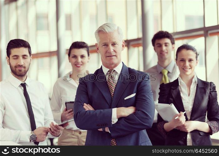 portrait of senior businessman as leader at modern bright office interior, young people group in background as team