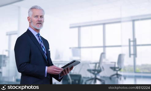 Portrait of senior businessman in front of his modern office with tablet. Senior businessman in his office