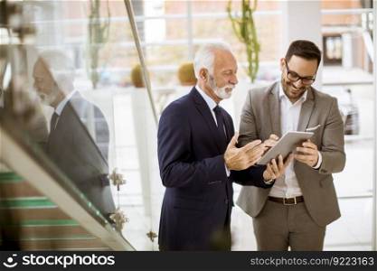 Portrait of senior businessman pointing and showing something to junior partner on digital  tablet at office