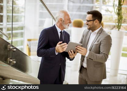 Portrait of senior businessman pointing and showing something to junior partner on digital  tablet at office