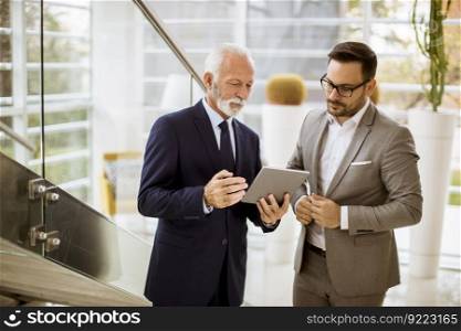 Portrait of senior businessman pointing and showing something to junior partner on digital  tablet at office