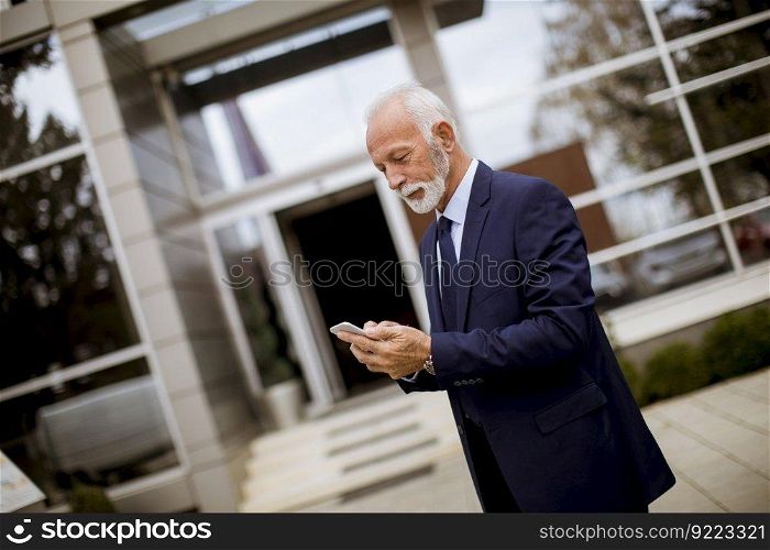 Portrait of senior businessman using mobile phone in front of office building