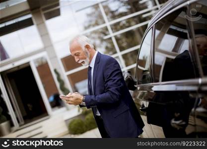 Portrait of senior businessman using mobile phone near car
