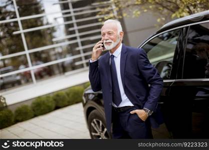 Portrait of senior businessman using mobile phone near car
