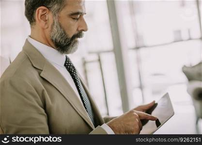 Portrait of senior businessman with digital tablet standing in office
