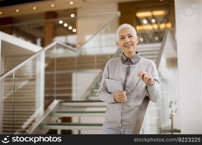 Portrait of senior businesswoman standing in modern office and holding digital tablet