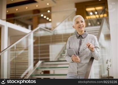 Portrait of senior businesswoman standing in modern office and holding digital tablet