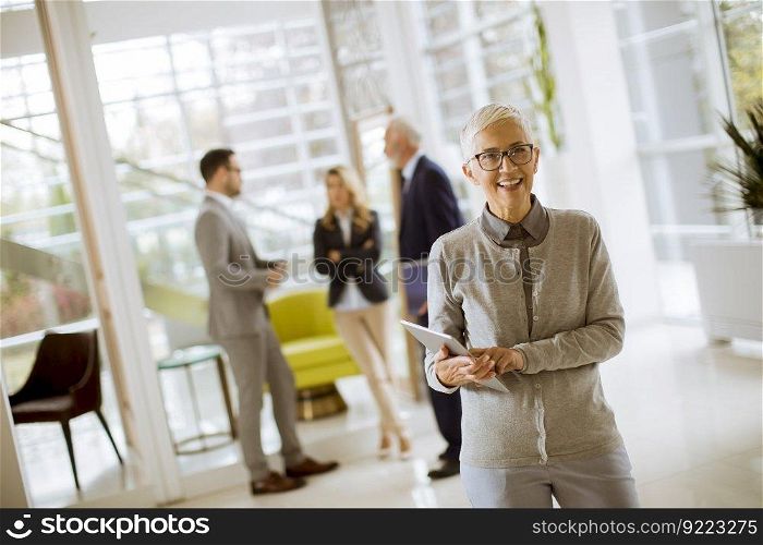 Portrait of senior businesswoman standing with digital tablet while other business people standing in background