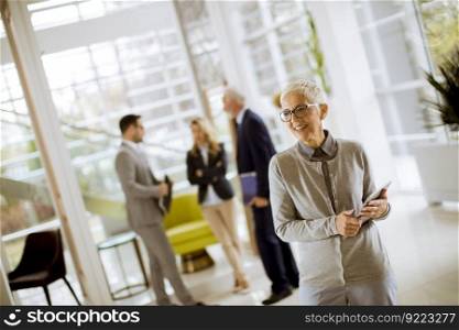 Portrait of senior businesswoman standing with digital tablet while other business people standing in background