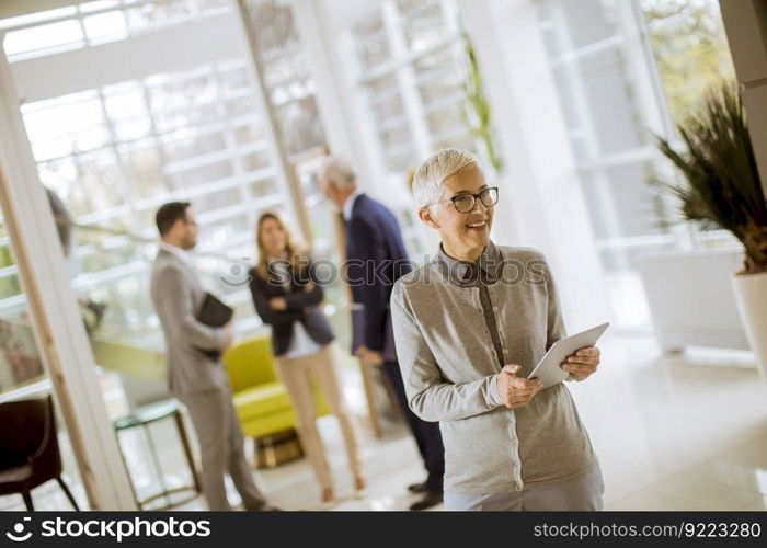 Portrait of senior businesswoman standing with digital tablet while other business people standing in background