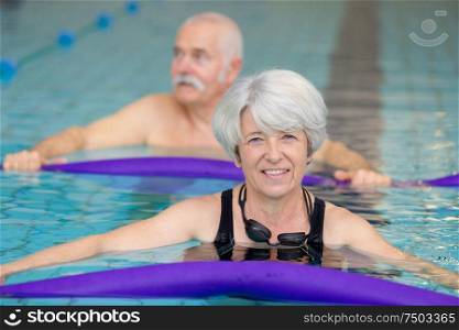portrait of senior couple exercising with noodles in pool
