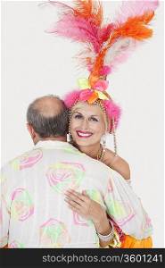 Portrait of senior couple in Brazilian outfits dancing over gray background
