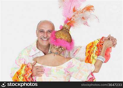 Portrait of senior couple in Brazilian outfits dancing over gray background