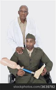Portrait of senior doctor standing with military officer holding artificial limb as he sits in wheelchair over gray background