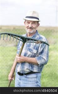 Portrait of senior farmer in plaid shirt holding rake at farm