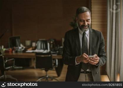 Portrait of senior handsome businessman using cell phone in modern office