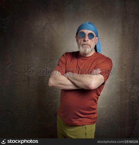portrait of senior, handsome man with gray beard in skull cap and round blue sunglasses, grunge urban environment
