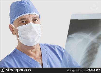 Portrait of senior male surgeon examining x-ray over gray background