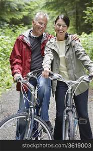 Portrait of senior man and middle-aged woman on bicycles in forest, smiling