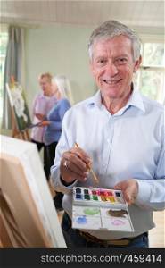 Portrait Of Senior Man Attending Painting Class With Teacher In Background