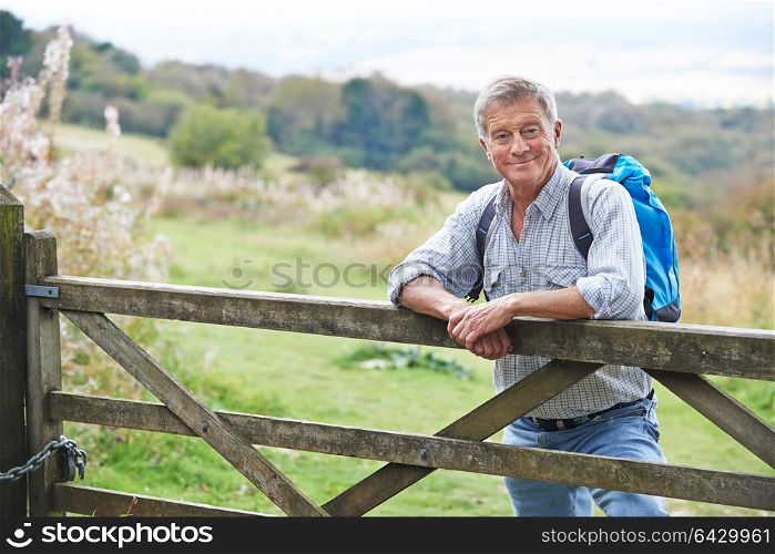 Portrait Of Senior Man On Hike In Countryside Resting By Gate