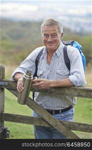 Portrait Of Senior Man On Hike In Countryside Resting By Gate And Having Hot Drink