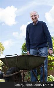 Portrait Of Senior Man Pushing Barrow Whilst Gardening