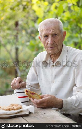 portrait of senior man sits in the garden and drinks tea with a pie