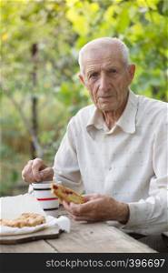 portrait of senior man sits in the garden and drinks tea with a pie
