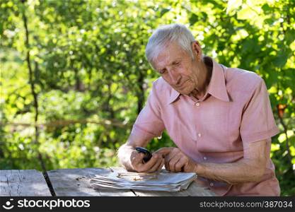 portrait of senior man sitting at a table in the garden and talking on the phone