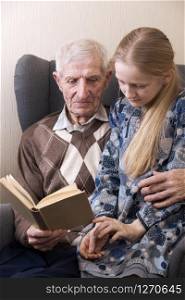 portrait of senior man sitting in an armchair together with granddaughter and reading books. leisure old man
