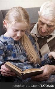 portrait of senior man sitting in an armchair together with granddaughter and reading books. leisure old man